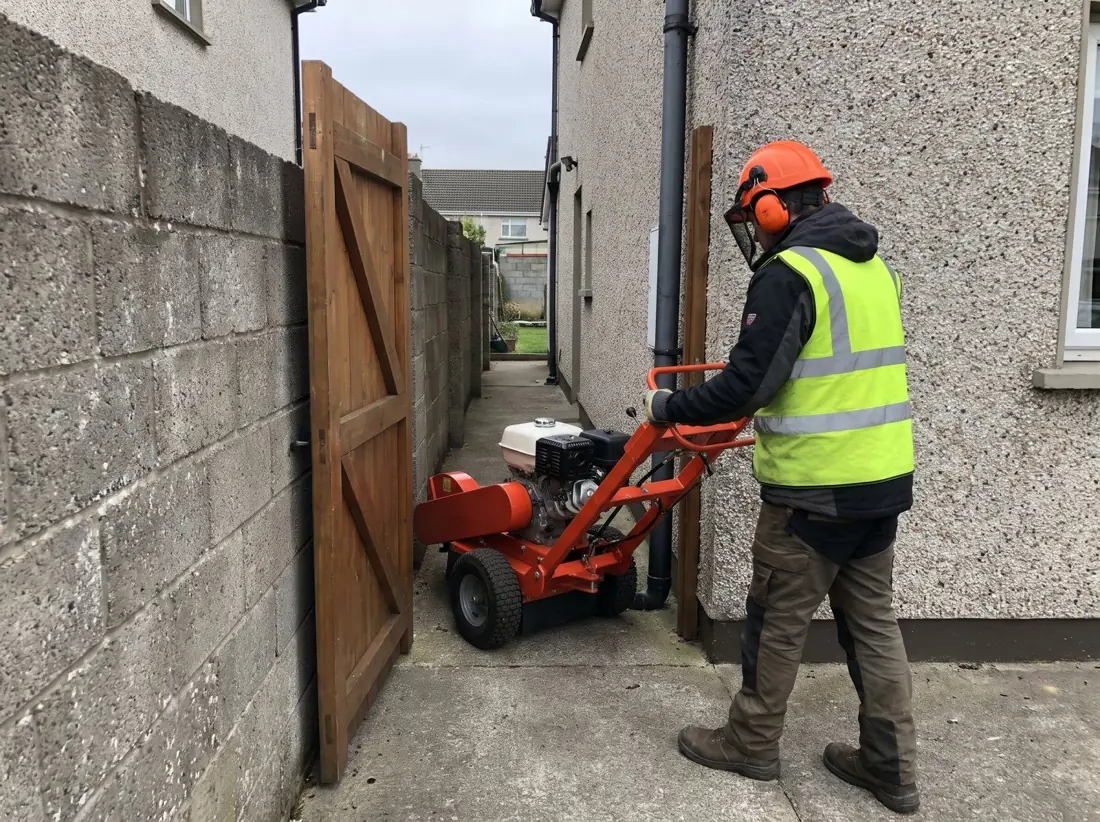 Compact walk-behind stump grinder going through a narrow side gate